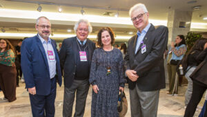 Quatro pessoas, sendo três homens e uma mulher, com roupas sociais, posando para a foto e sorrindo.