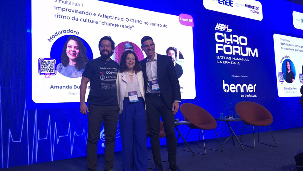Os três participantes do painel posam lado a lado no palco.