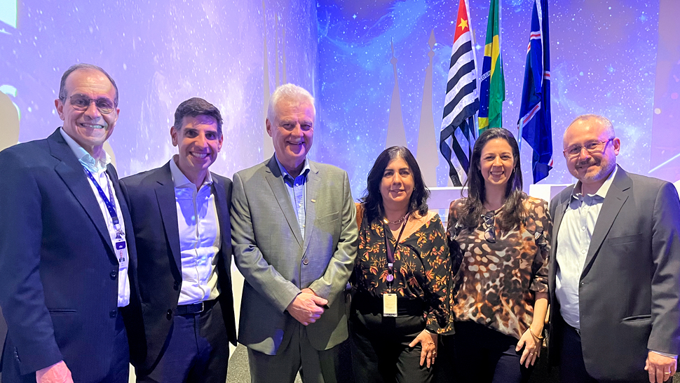 Seis superintendentes do CIEE posam sorrindo para a foto. Quatro homens e duas mulheres estão alinhados, vestindo trajes sociais. Ao fundo, há projeções em tons de azul e roxo, além das bandeiras do Brasil e do estado de São Paulo.